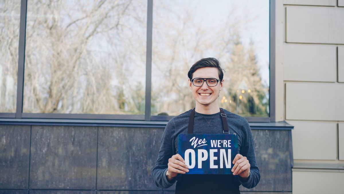 Small business owner holding an open sign outside a shop
